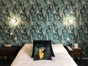A hotel room with a bed, two nightstands, and a wall with a tropical leaf pattern.