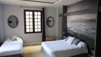 A bedroom with two beds, a large window, and a wall-mounted painting.