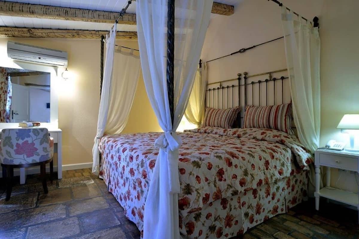 A bedroom with a four-poster bed, a bedside table with a lamp, and a chair with a floral pattern.
