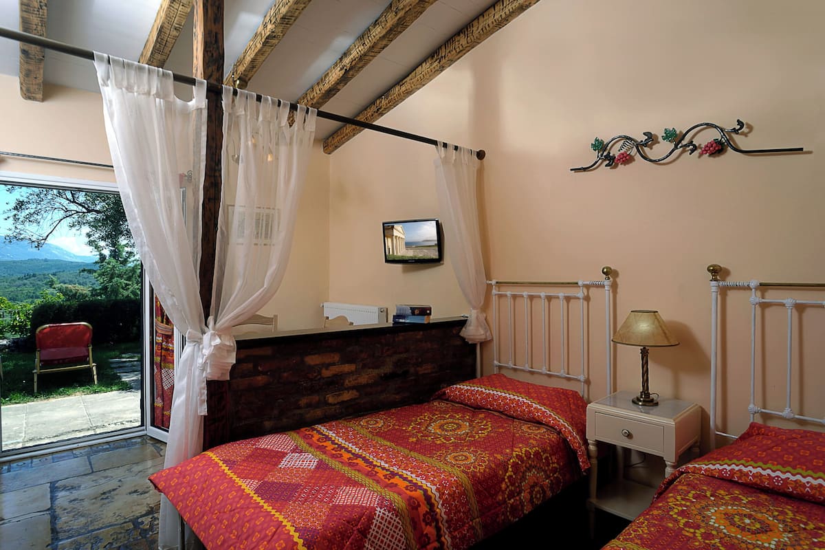 A bedroom with a bed, a nightstand, a lamp, a TV, and a view of the outdoors.