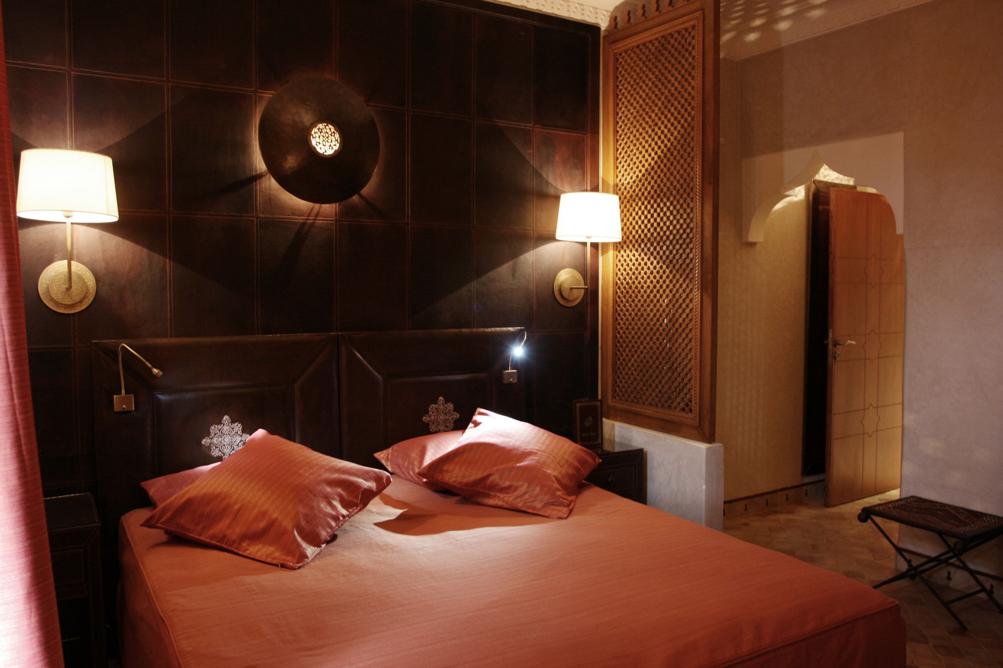 A hotel room with a large bed, two bedside lamps, a decorative wall panel, and a wooden door.