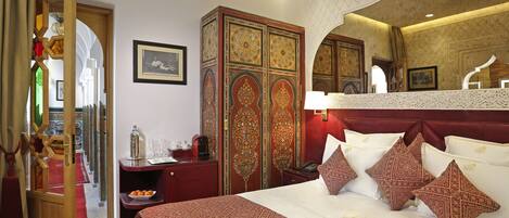 A hotel room with a large bed, a red and white patterned bedspread, a wooden wardrobe, and a red carpet.