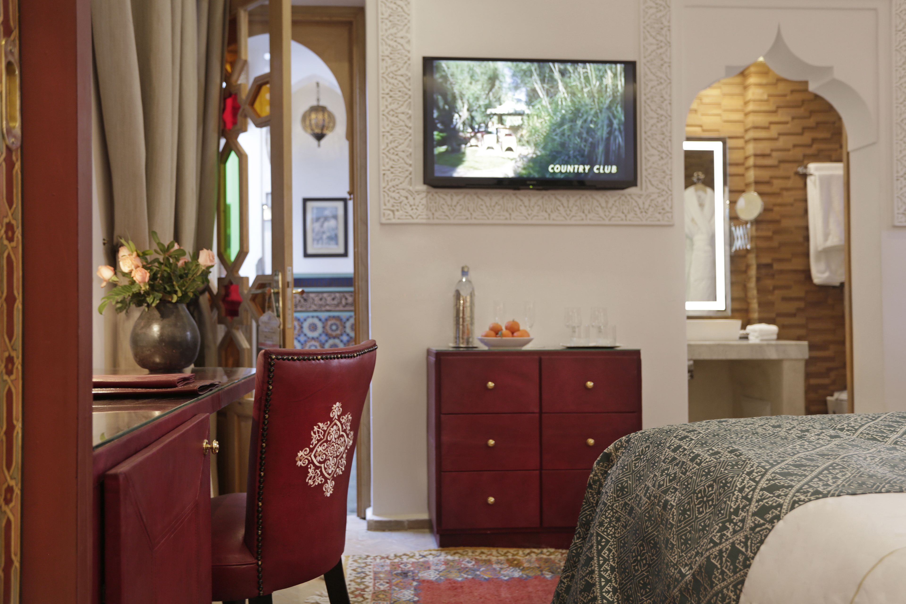 A hotel room with a bed, a TV mounted on the wall, a red chair, a wooden cabinet, and a mirror.