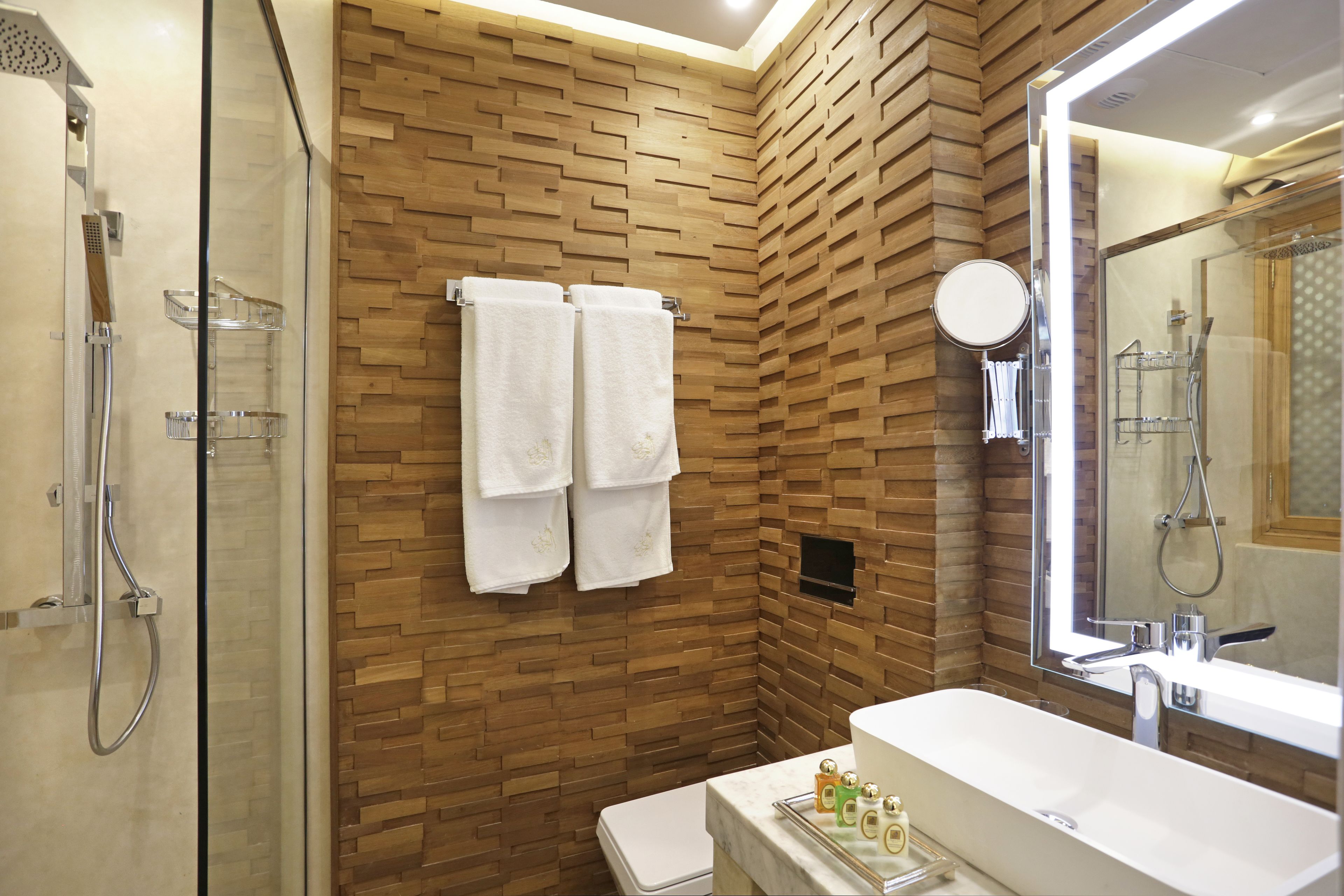 A modern bathroom with a wooden wall, a glass shower enclosure, a white sink, and a large mirror.