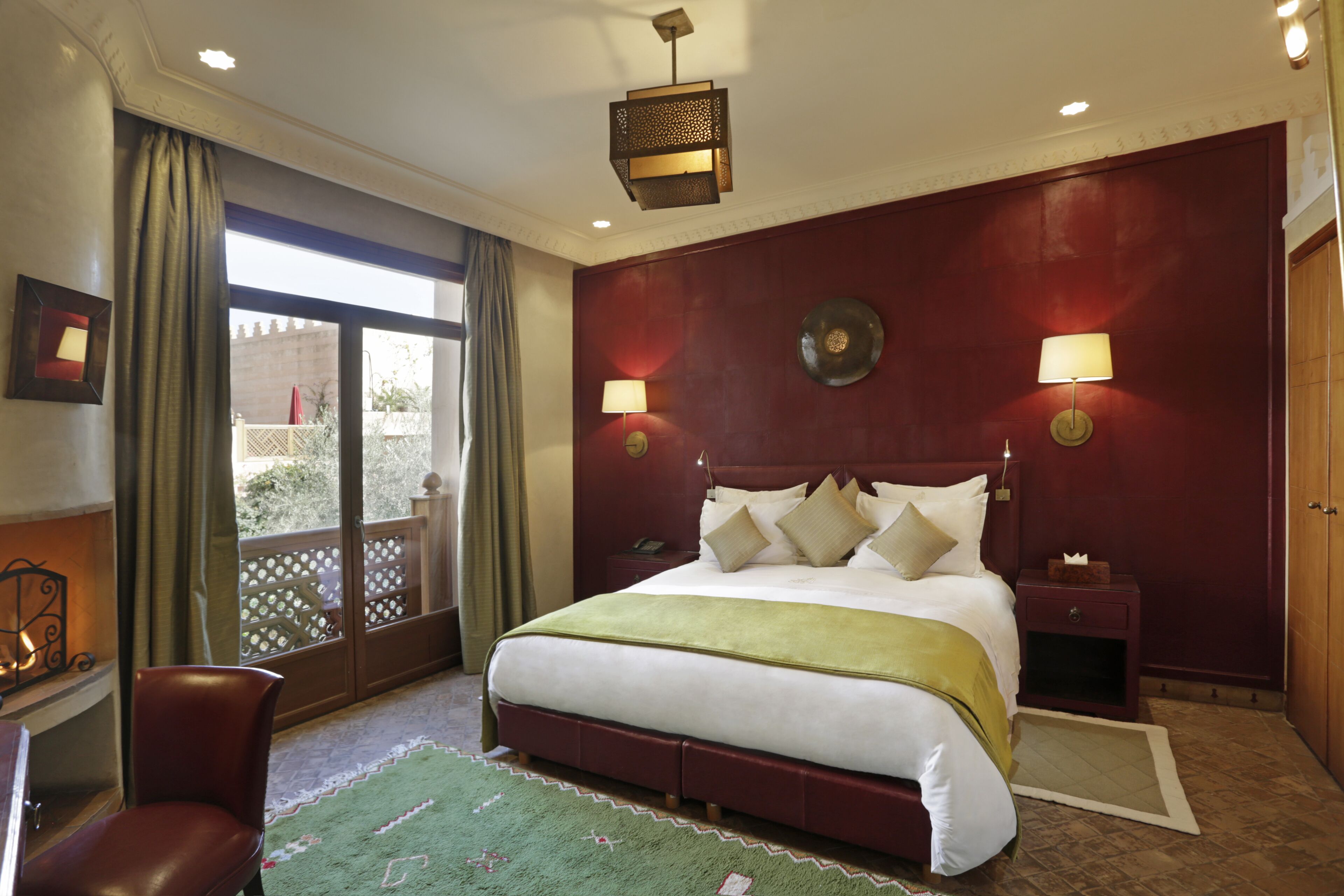 Une chambre d’hôtel avec un grand lit, deux lampes de chevet, une table de chevet, une chaise et une vue sur l’extérieur, accessible par une porte coulissante.