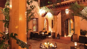 Un patio interior con arquitectura tradicional, que incluye arcos y balcones de madera, amueblado con sofás y mesas, y decorado con plantas y velas.