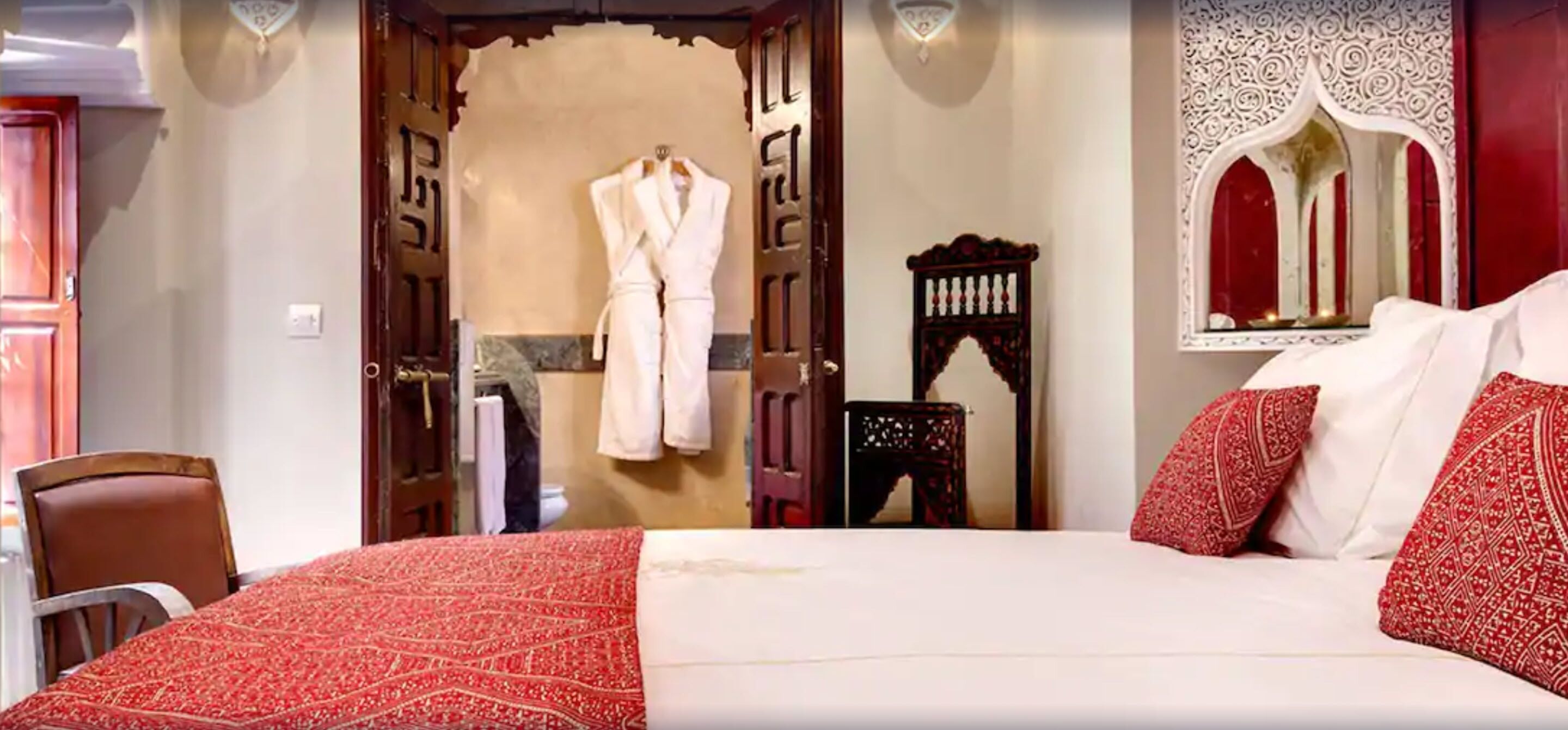A hotel room with a large bed, a wooden wardrobe, a mirror, and a red patterned bedspread.