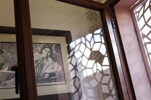 A framed portrait on a wall, a wooden door, and a patterned window.