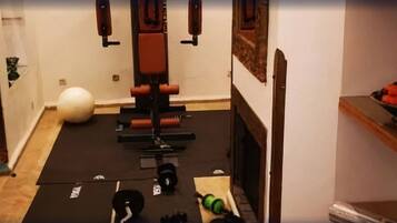 Une salle de sport à domicile équipée de matériel d’exercice, d’un tapis de yoga et d’un saladier de fruits posé sur une étagère.