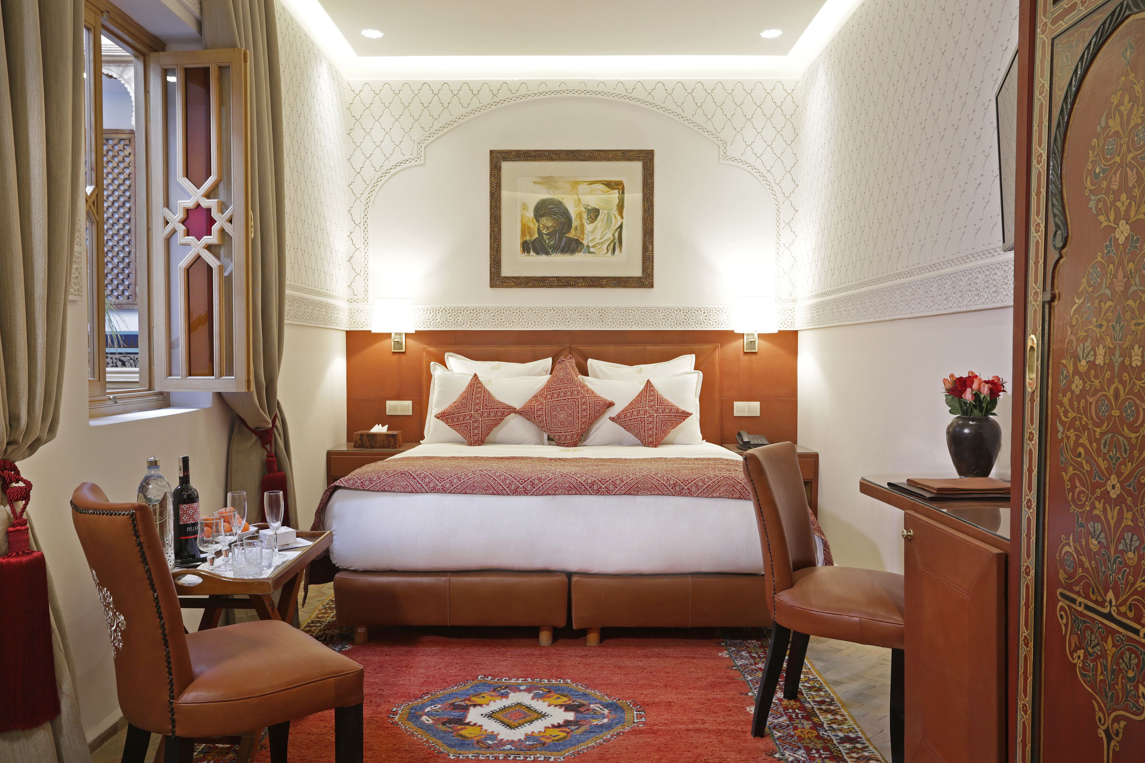 Hotelkamer met een groot bed, een eettafel, twee stoelen, een klein tafeltje met een vaas en een decoratief wandobject.