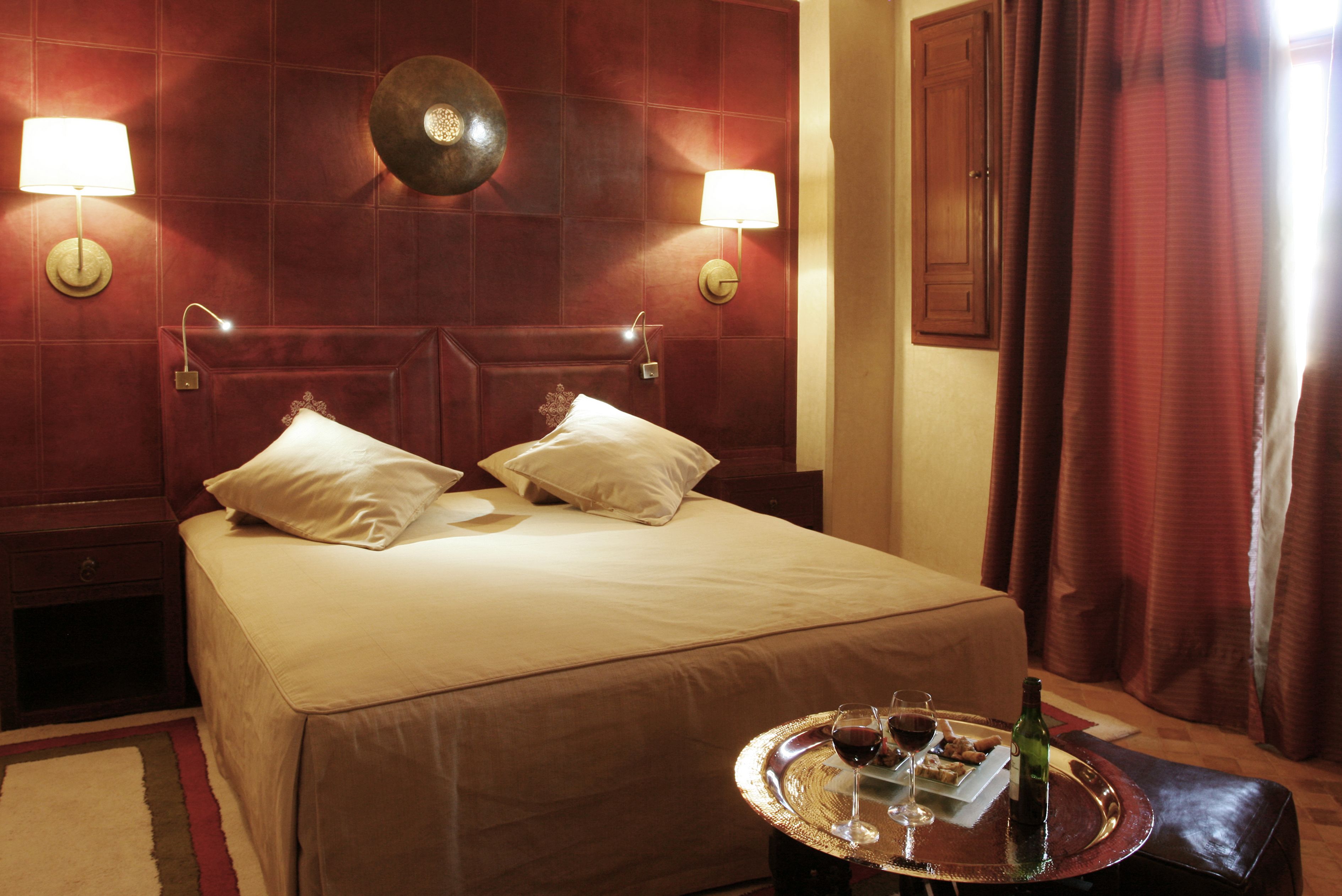 A hotel room with a large bed, two bedside lamps, a wall clock, and a tray with a bottle and glasses on the nightstand.