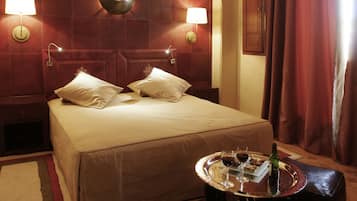 A hotel room with a large bed, two bedside lamps, a wall clock, and a tray with a bottle and glasses on the nightstand.