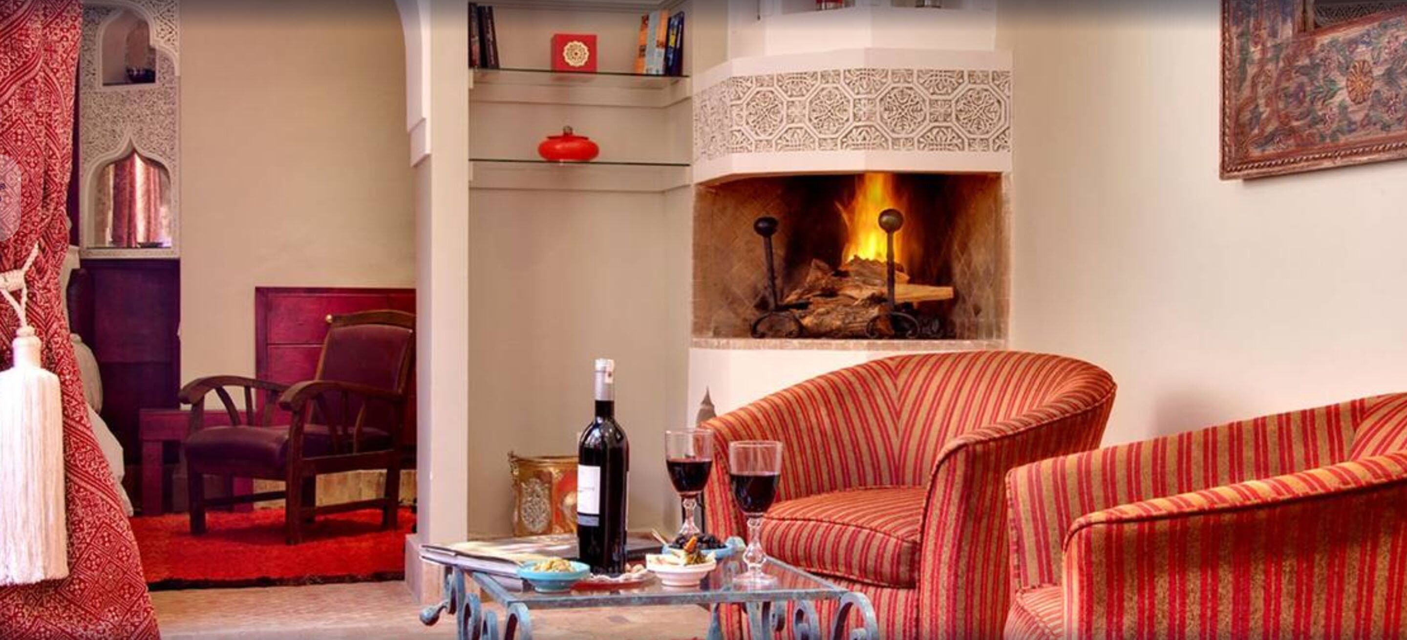 A cozy living room with a fireplace, striped armchairs, a coffee table, and a bookshelf.