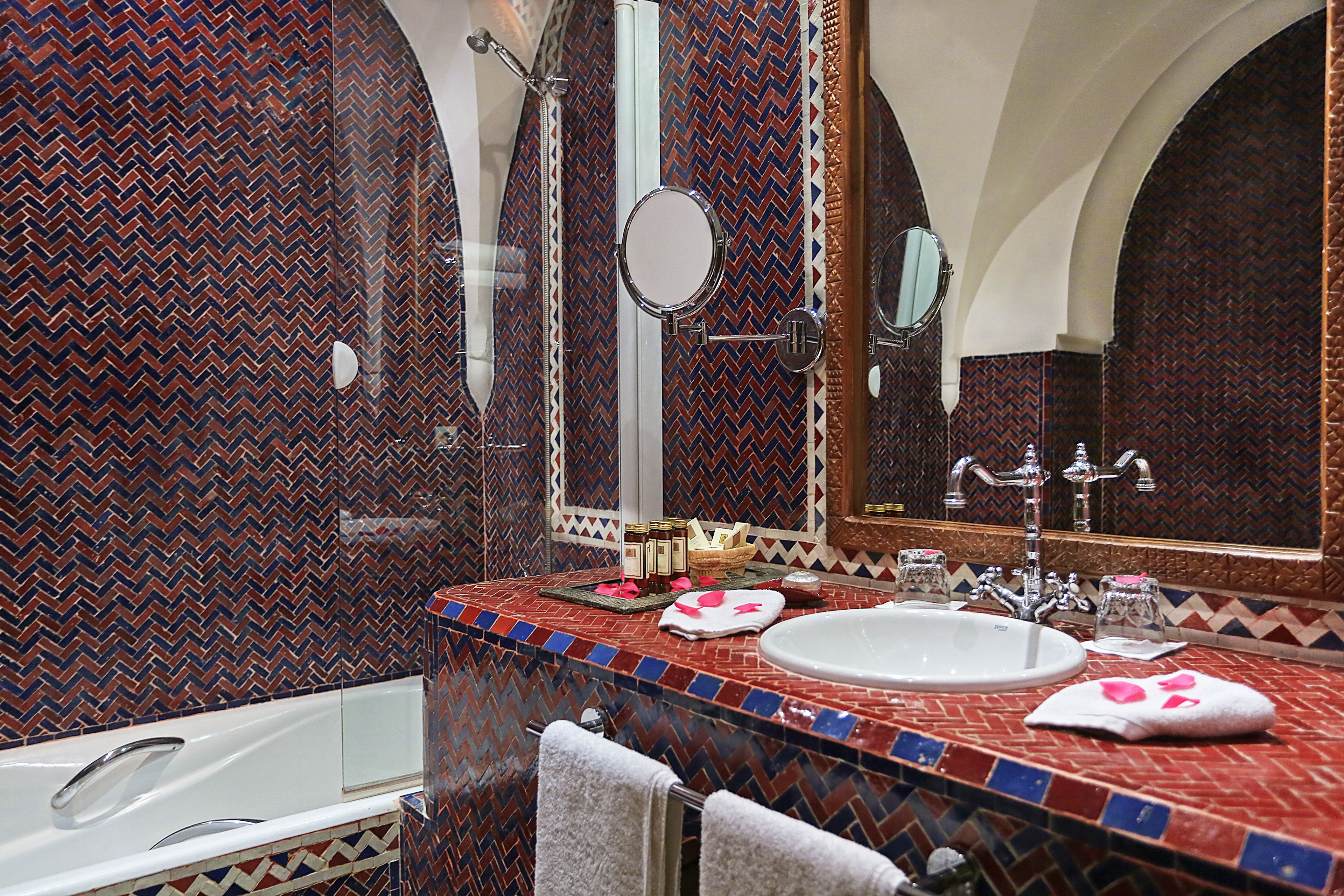 A bathroom with a herringbone patterned tile wall, a white sink, a mirror, and a bathtub.