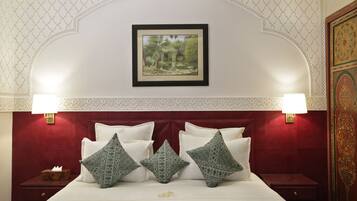 A hotel room with a red headboard, white bedding, and decorative pillows. There is a framed picture on the wall above the bed and two wall-mounted lamps on either side.