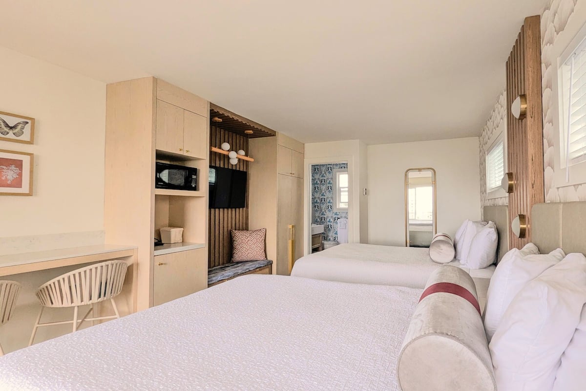 Quarto de hotel com duas camas, uma escrivaninha com cadeira, micro-ondas e televisão.