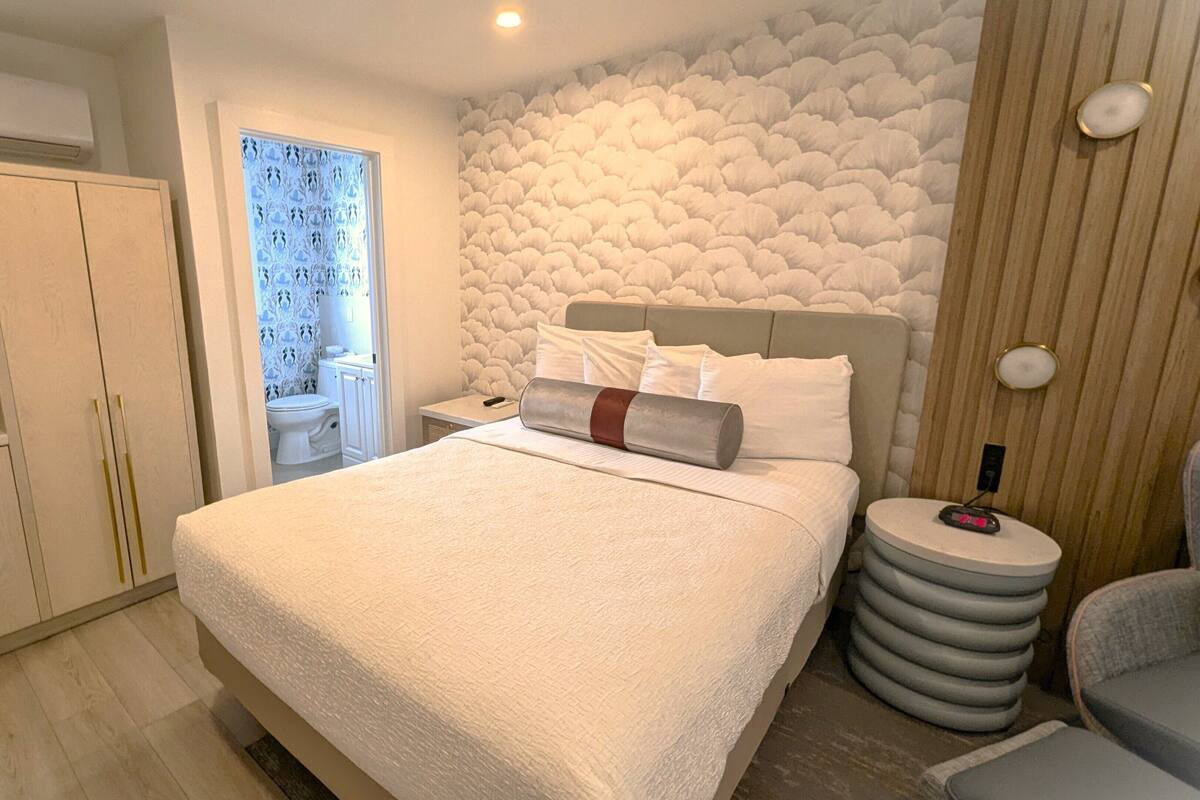 Quarto com cama, mesa de cabeceira, cadeira, micro-ondas e armário.