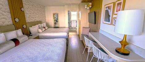 Et hotelværelse med to senge, et skrivebord med stole, et spejl og et fjernsyn på væggen.