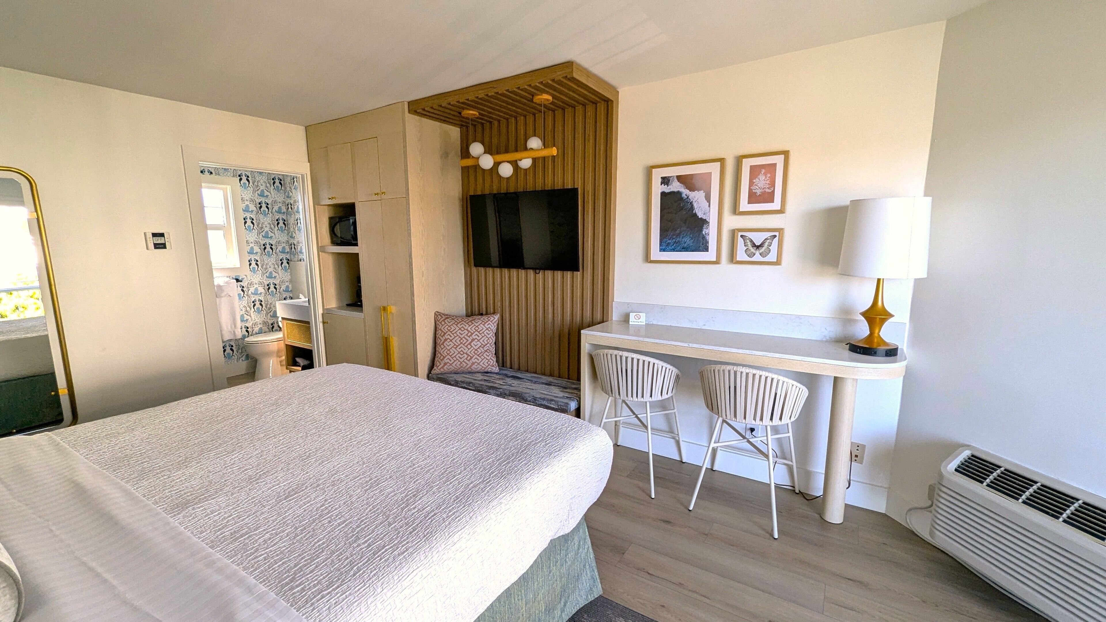 A hotel room with a bed, a desk with two chairs, a television, and a heater.
