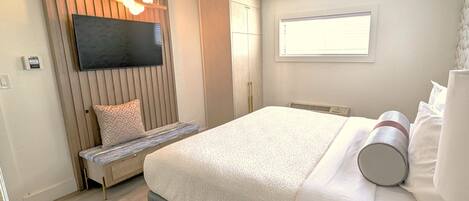 A modern bedroom with a bed, a bench, a TV, and a window.