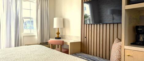 A hotel room with a bed, a desk, a chair, a TV mounted on the wall, and a coffee machine.