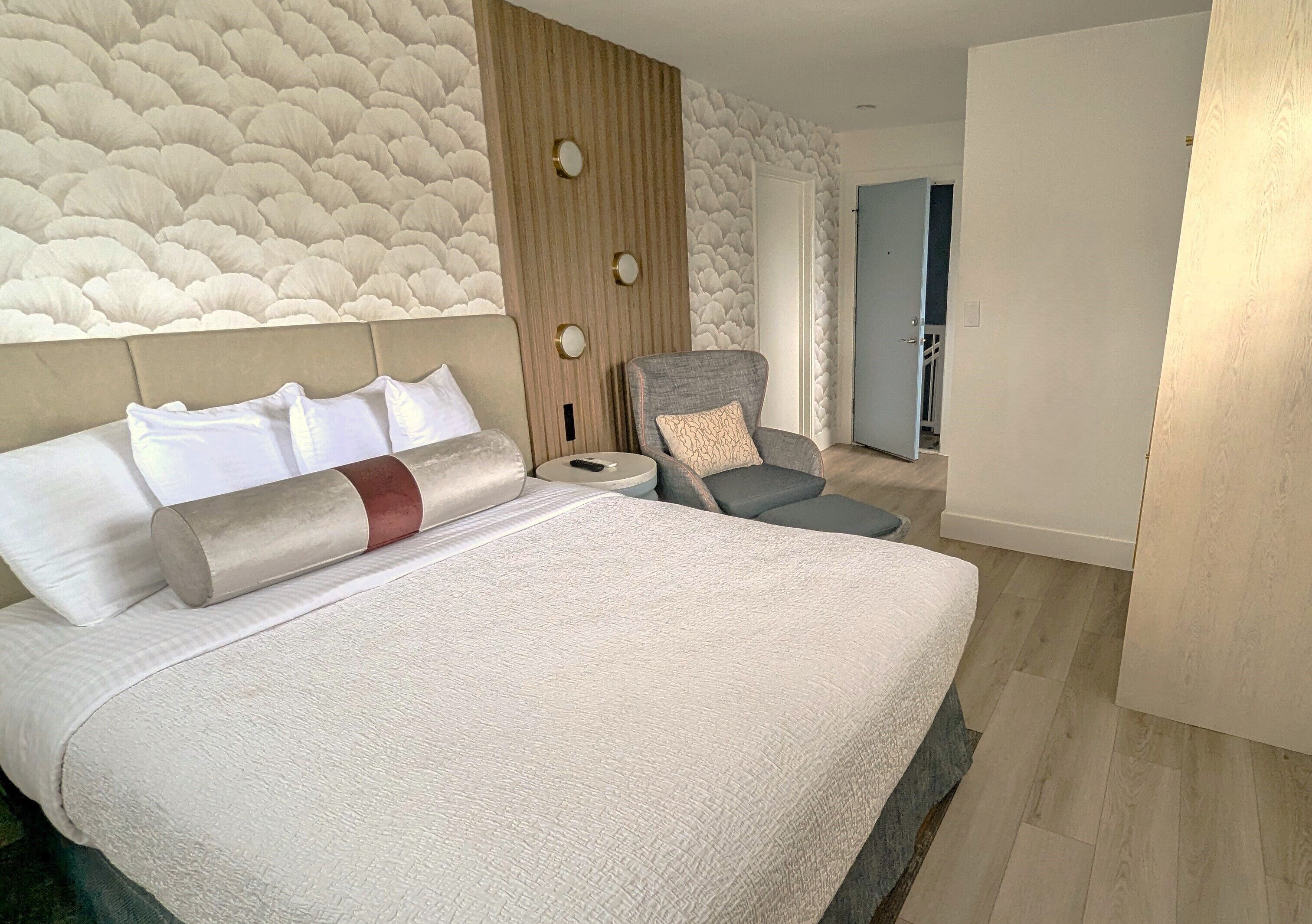 Un dormitorio con una cama grande, cabecera de madera, un sillón gris y pared con diseño.