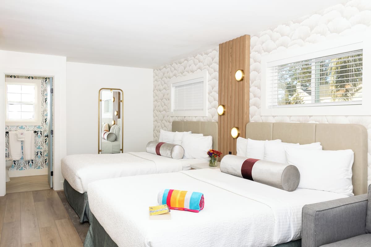 Quarto de hotel com duas camas, um espelho, uma janela com persianas e uma parede de destaque em madeira.