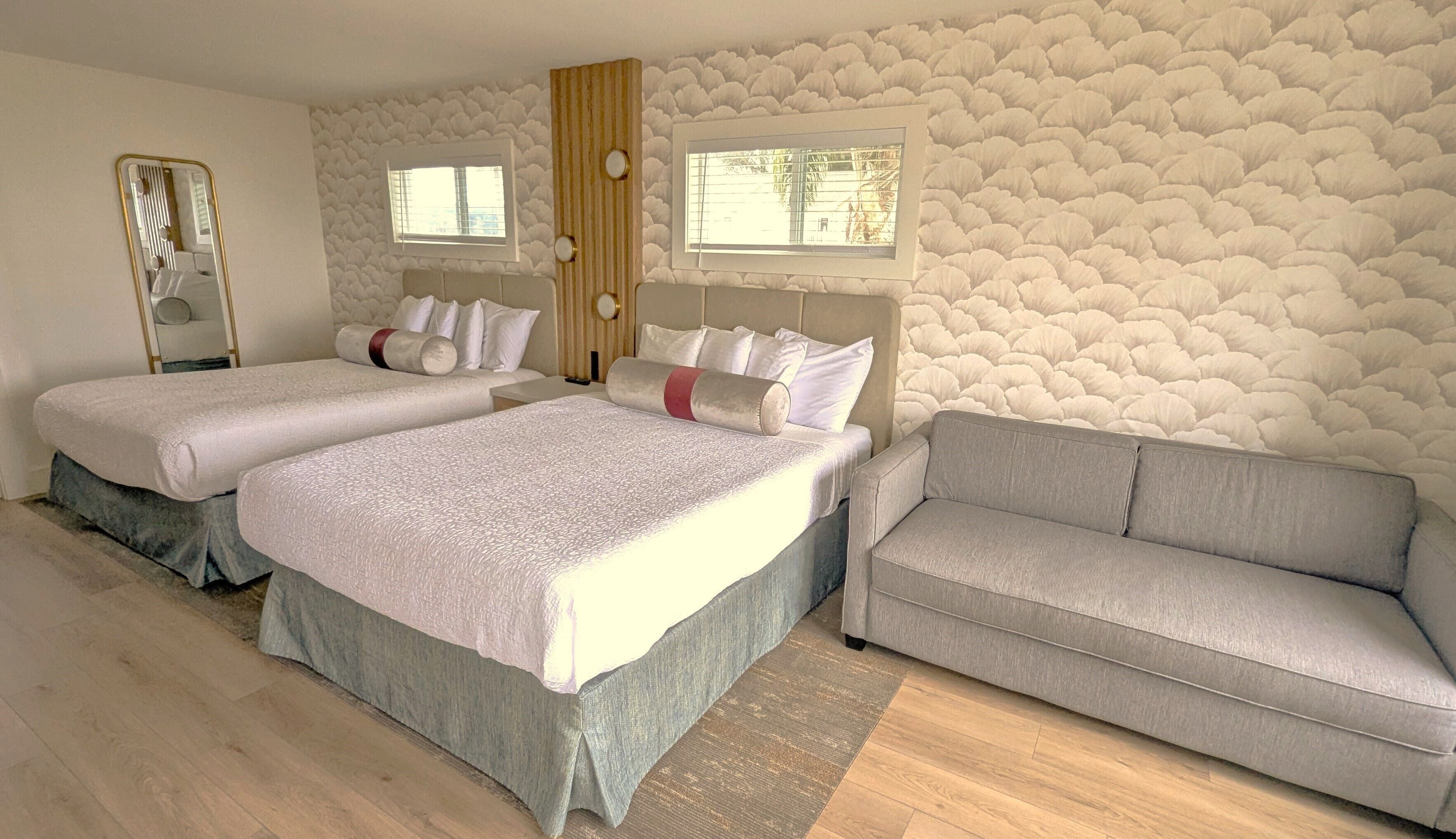 A hotel room with two beds, a sofa, a mirror, and a stone-patterned wall.