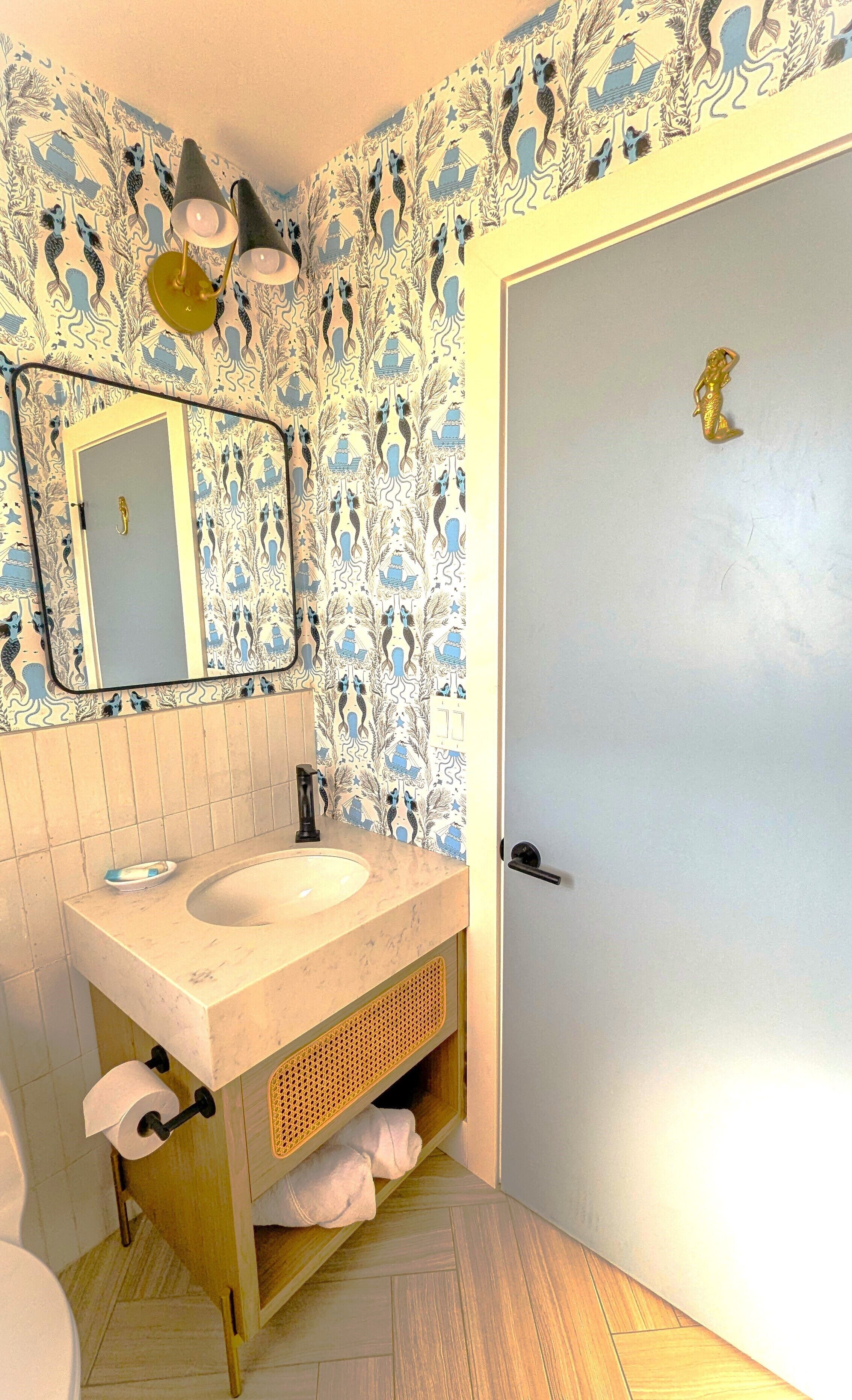 Un baño con lavamanos, espejo y papel tapiz estampado.