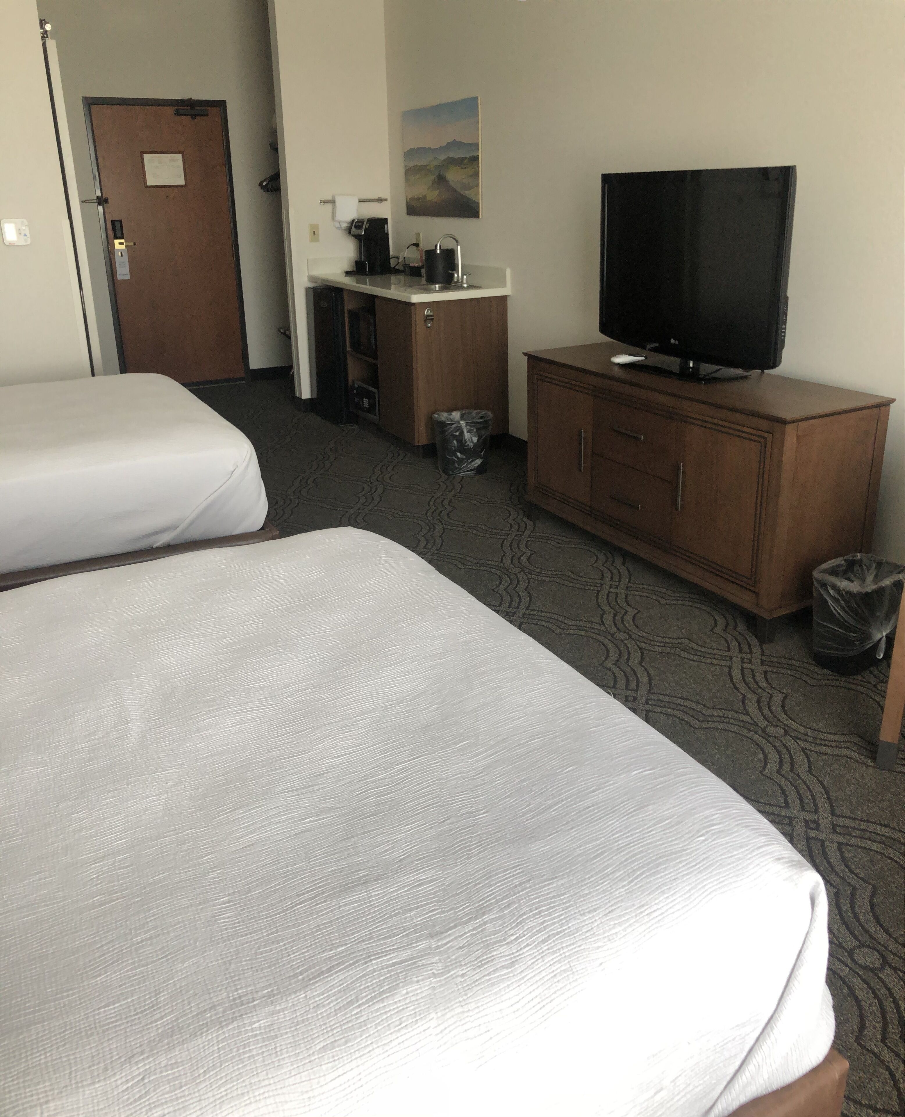 A hotel room with two beds, a television, a coffee maker, and a painting on the wall.