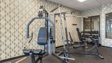 A gym with weightlifting equipment, a bench, and a wall of dumbbells.