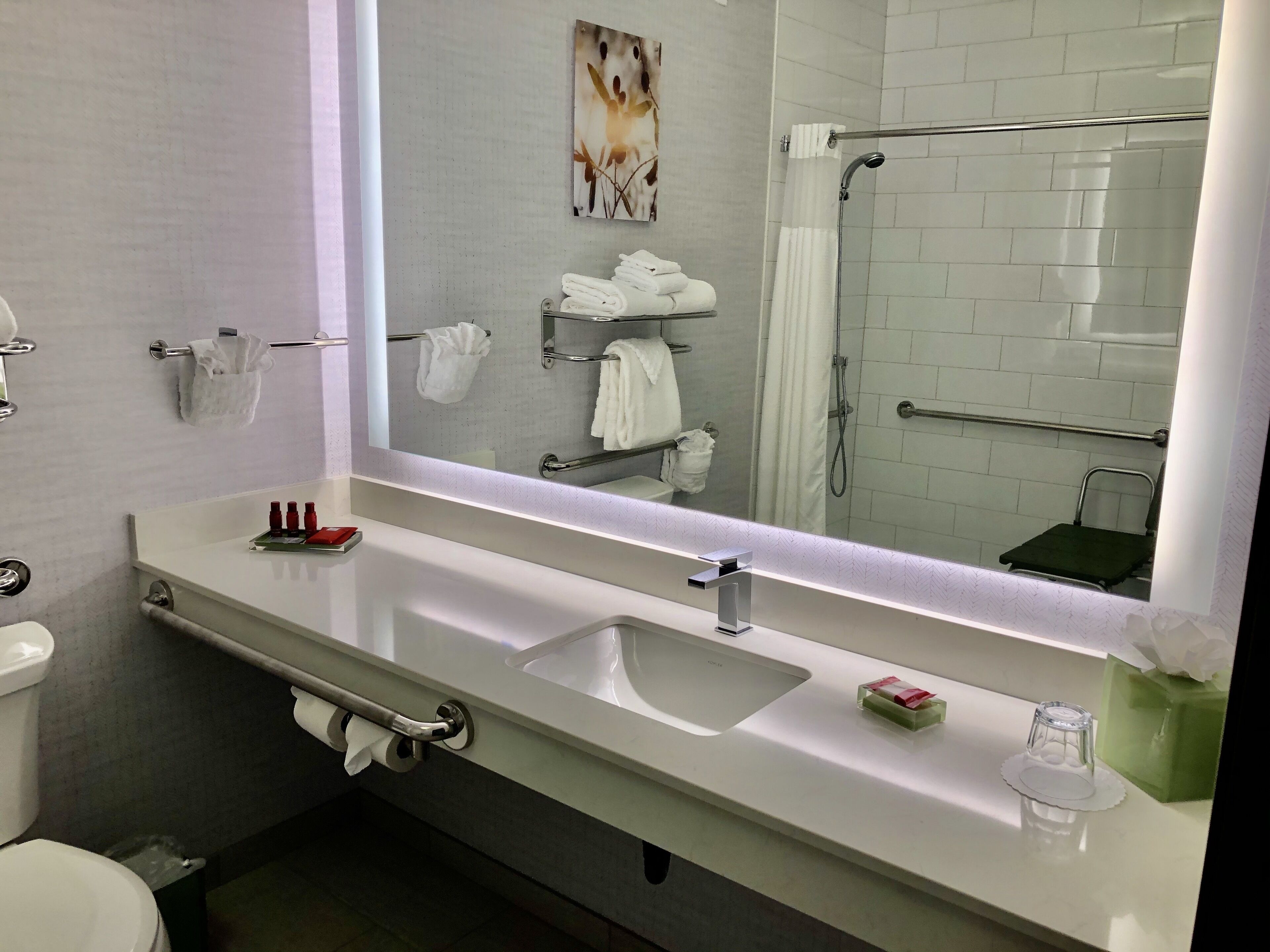 A modern bathroom with a white sink, a large mirror, and a shower area.