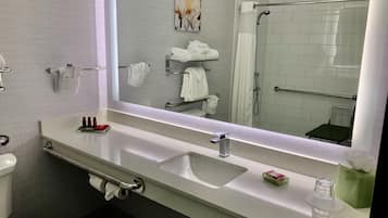 A modern bathroom with a white sink, a large mirror, and a shower area.