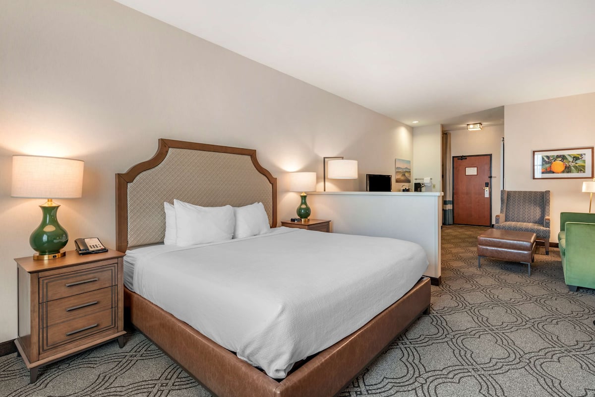 A hotel room with a large bed, bedside tables, a desk, a chair, and a small table with a lamp.