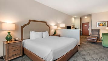 A hotel room with a large bed, bedside tables, a desk, a chair, and a small table with a lamp.