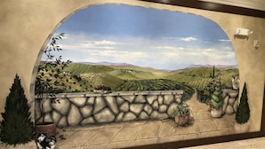 Une fresque représentant un paysage de vignoble, avec un mur de pierres et des plantes en pot.