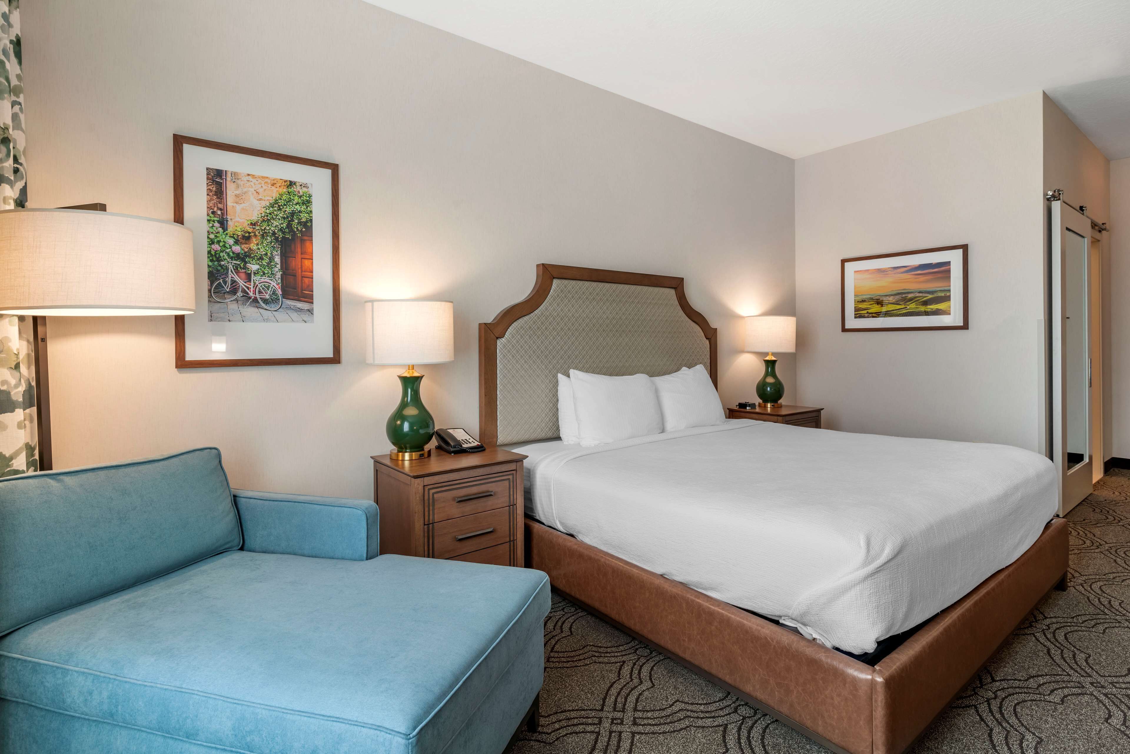 A hotel room with a bed, a blue sofa, two bedside tables with lamps, and framed pictures on the walls.
