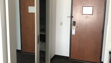 A hallway with a carpeted floor, a wooden door with a plaque, and a mirror reflecting part of the room.