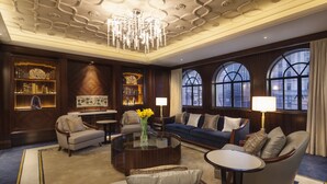 Un salon luxueux avec un grand canapé, des fauteuils, une table basse et un lustre. On y trouve également des étagères et une vue à travers de grandes fenêtres en arc de cercle.