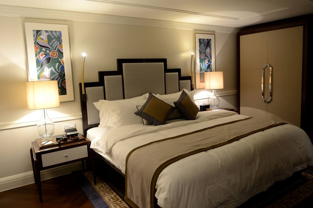 A neatly made bed with white linens and two pillows, flanked by bedside tables with lamps and a phone.