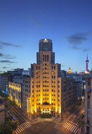 A large, multi-story building with a prominent entrance and a clock tower in the background. - Metropolo Xin Cheng Hotel, The Bund Shanghai (Shanghai)
