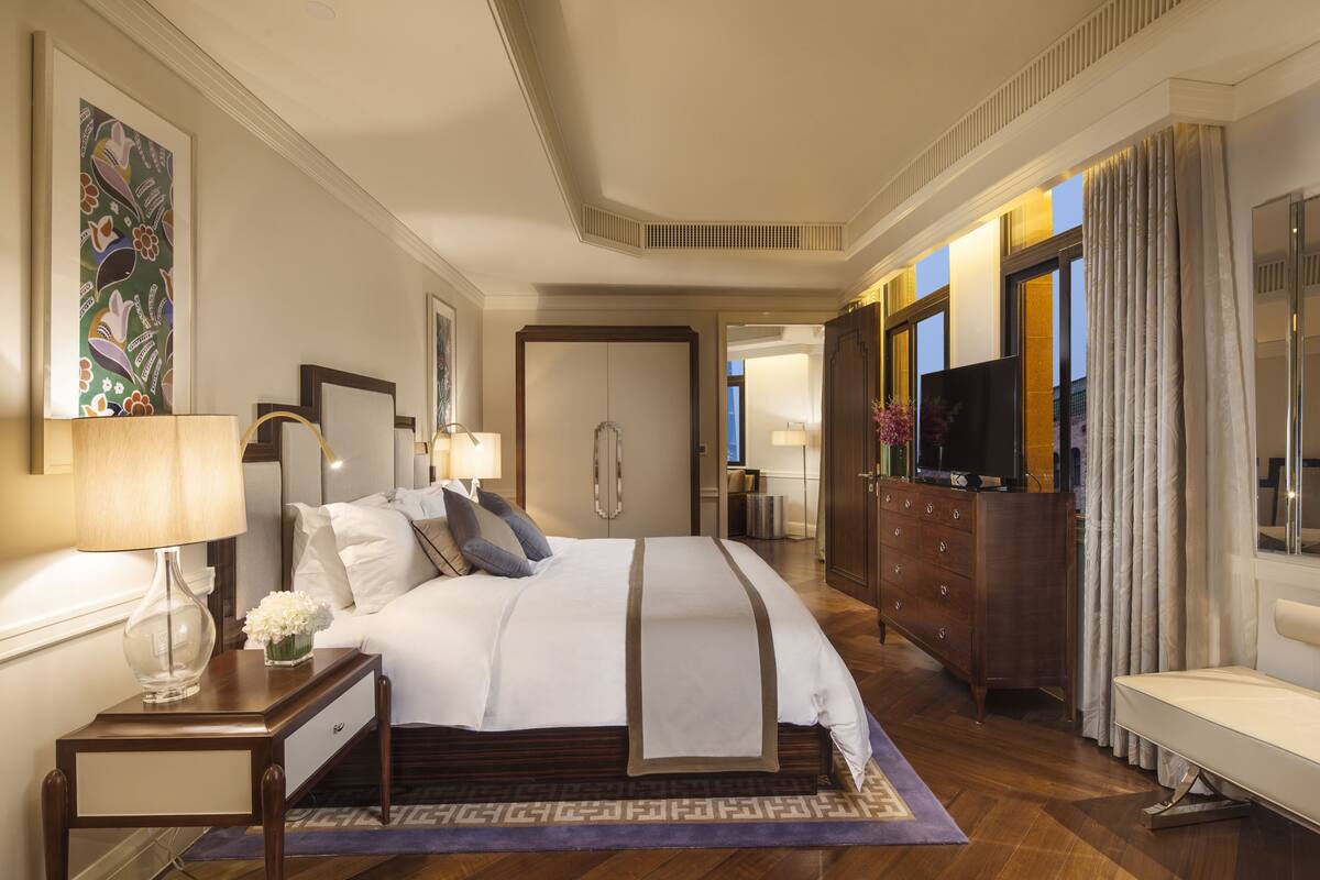A hotel room with a large bed, bedside tables, a TV, a wardrobe, and a bathroom visible through an open door.