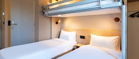 A hotel room with two single beds, a wooden headboard, bedside lamps, and a door with a handle.