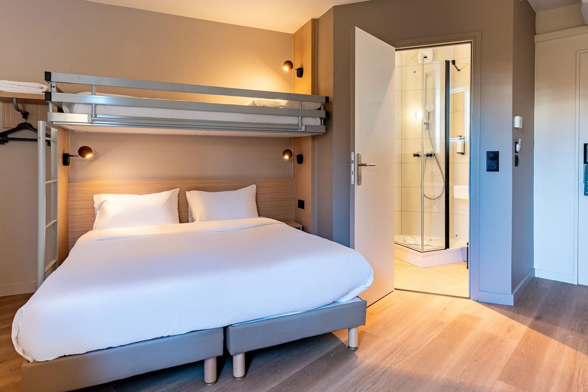 Una camera d'albergo moderna con un letto a castello, zona doccia e pavimento in legno.