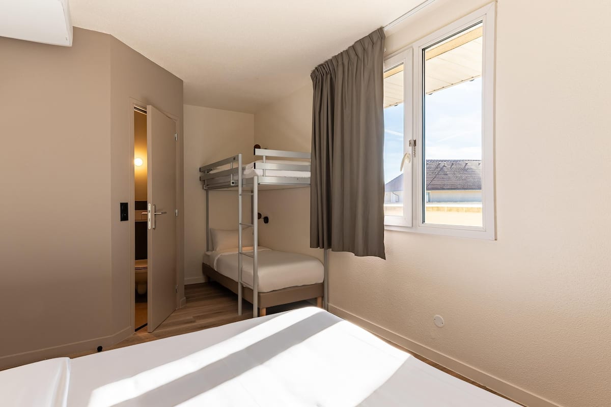 Una camera con un letto a castello, una finestra, una porta che conduce al bagno e vista su un edificio.