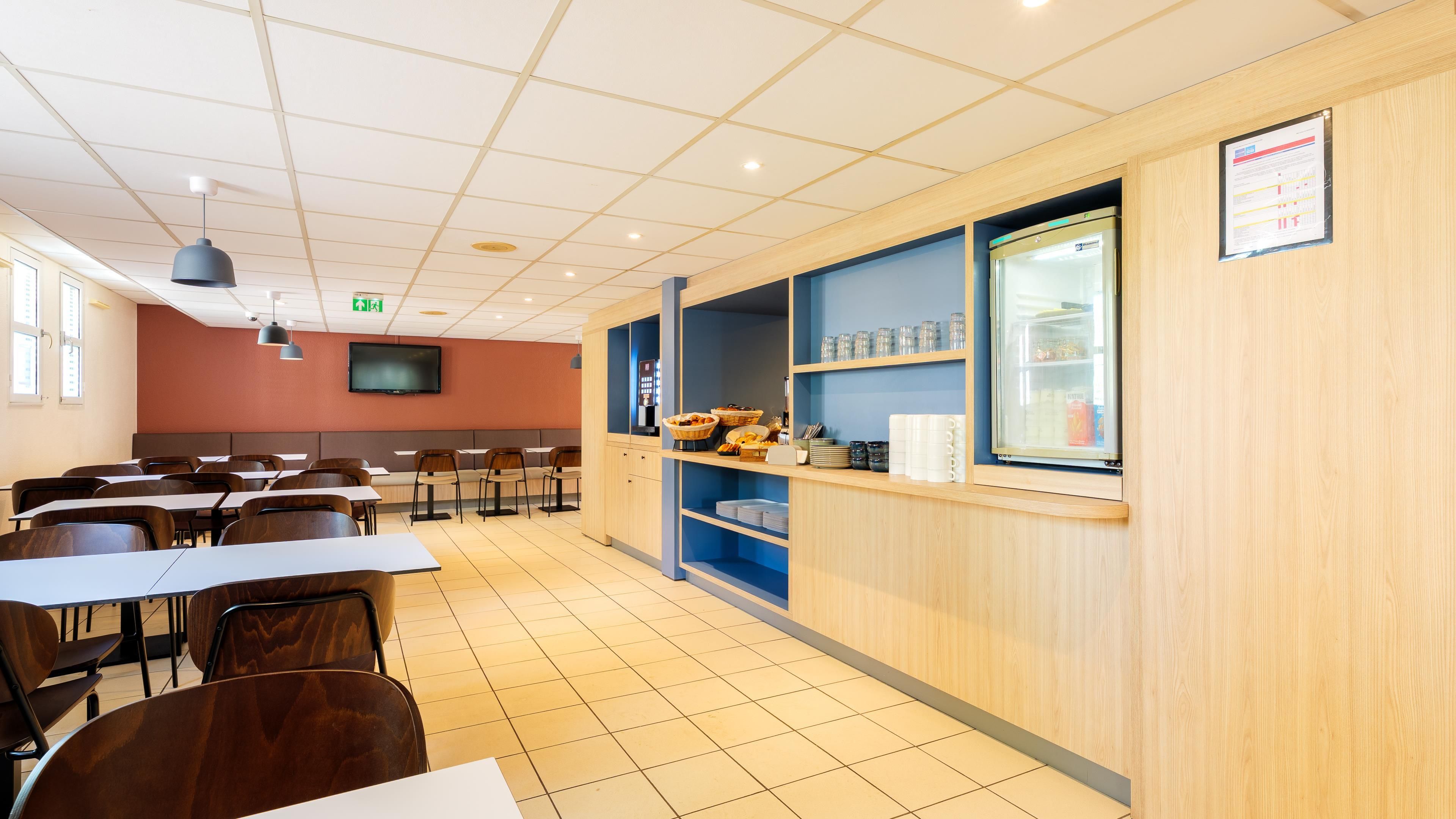 Cafetería con mesas y sillas, un televisor y un refrigerador con alimentos.