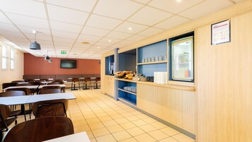 Cafetería con mesas y sillas, un televisor y un refrigerador con alimentos.
