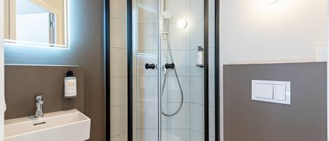 A modern bathroom with a glass-enclosed shower, a white sink, and a hand soap dispenser.