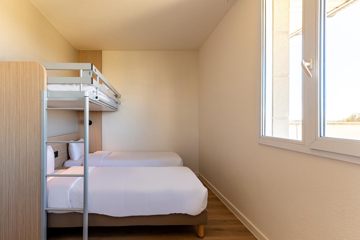 Una stanza piccola e compatta con un letto a castello e un letto singolo, una finestra con vista e una porta in legno.