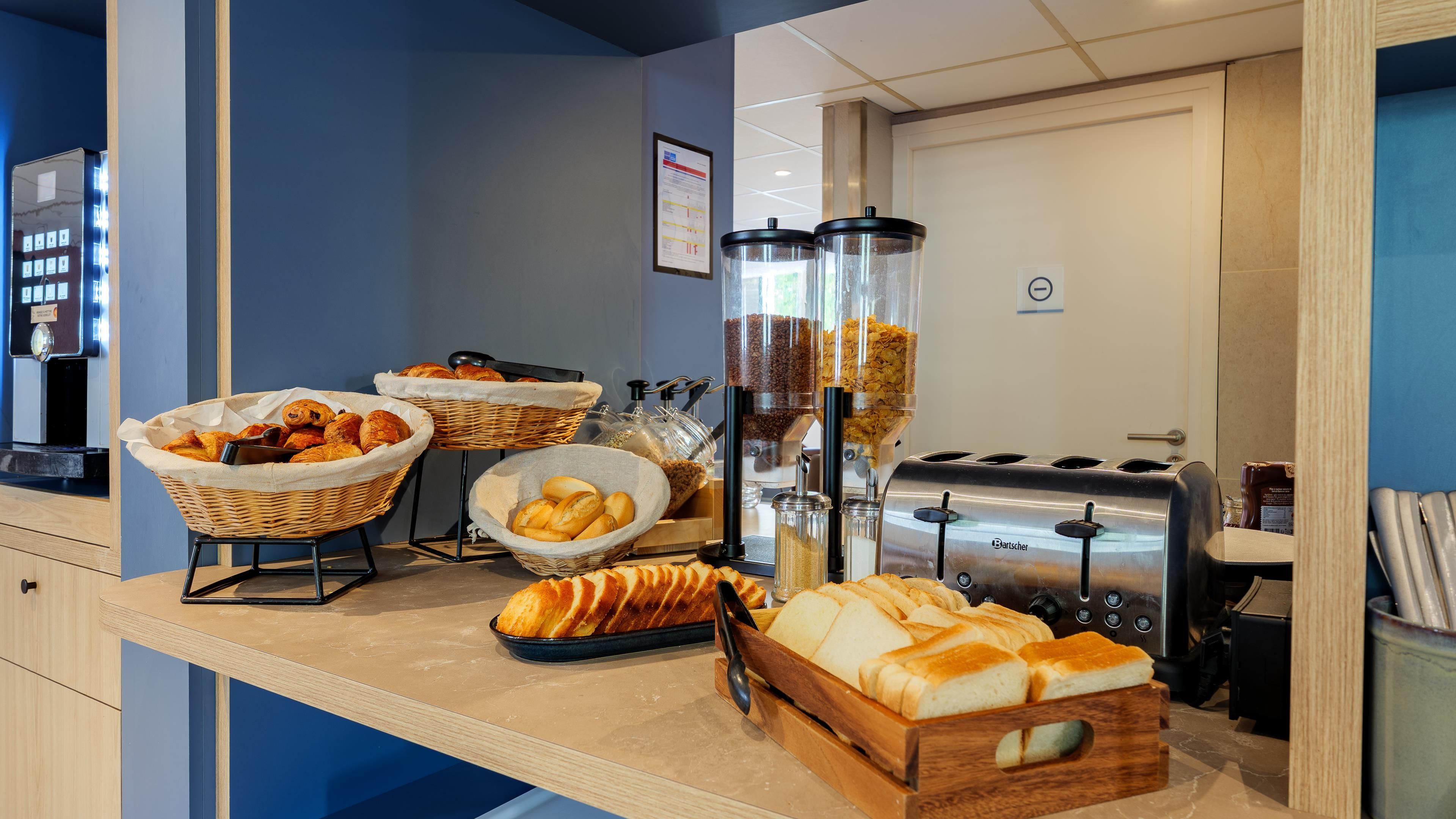A breakfast buffet with various breads and pastries, a coffee machine, and a toaster.